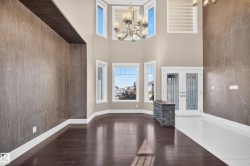 Grand foyer featuring double entry doors with decorative glass inserts, a multi-tiered chandelier, a stone-clad half-wall, wood-finish flooring, and a bay window configuration providing abundant natural light - 