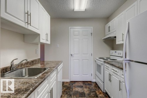 Bright kitchen featuring white cabinetry, a double basin stainless steel sink, patterned laminate countertops, white electric range, and a full-size white refrigerator - 5425 144B Avenue Northwest, Edmonton, AB - Indoor Photo Showing Kitchen
