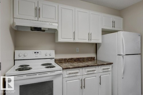 Kitchen featuring white cabinetry, a white electric range with an overhead vent, a white refrigerator, and a speckled countertop - 5425 144B Avenue Northwest, Edmonton, AB - Indoor Photo Showing Kitchen