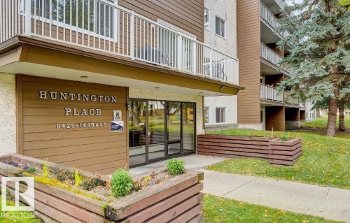 Apartment building entrance featuring a prominent "Huntington Place" sign, large glass entry doors, and a wood-paneled facade - 5425 144B Avenue Northwest, Edmonton, AB - Outdoor With Exterior