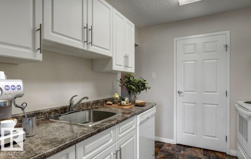 Bright kitchen featuring white cabinetry with dark hardware, a stainless steel sink, a dishwasher, and a paneled white door - 5425 144B Avenue Northwest, Edmonton, AB - Indoor Photo Showing Kitchen
