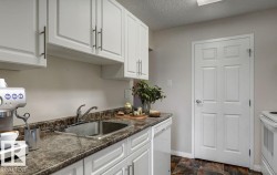 Bright kitchen featuring white cabinetry with dark hardware, a stainless steel sink, a dishwasher, and a paneled white door - 