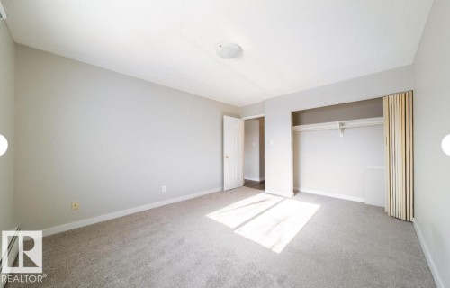 Spacious room featuring neutral carpeting, light gray wall paint, and a built-in closet with a hanging rod and shelf - 3312 105 Avenue Northwest, Edmonton, AB - Indoor Photo Showing Other Room