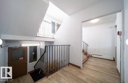 Multi-level interior featuring wood-finish flooring, white walls, black metal railings, and natural light from exterior window panels - 3312 105 Avenue Northwest, Edmonton, AB - Indoor Photo Showing Other Room