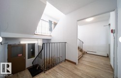 Multi-level interior featuring wood-finish flooring, white walls, black metal railings, and natural light from exterior window panels - 