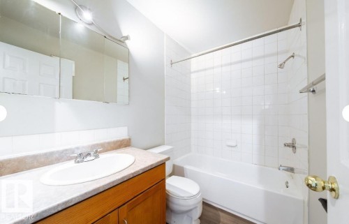Bathroom featuring a white bathtub, ceramic tile shower surround, wood-finish flooring, and a vanity with a laminate countertop - 3312 105 Avenue Northwest, Edmonton, AB - Indoor Photo Showing Bathroom