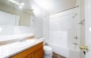 Bathroom featuring a white bathtub, ceramic tile shower surround, wood-finish flooring, and a vanity with a laminate countertop - 3312 105 Avenue Northwest, Edmonton, AB  - Indoor Photo Showing Bathroom 