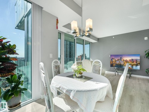 Floor-to-ceiling windows, light wood-finish flooring, recessed lighting, contemporary chandelier, and a neutral grey accent wall - #1501 10180 103 St Nw, Edmonton, AB - Indoor Photo Showing Dining Room