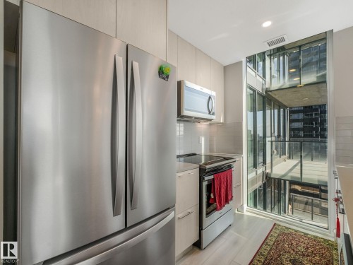 Kitchen featuring stainless steel appliances, light-toned cabinetry, tile backsplash, and an expansive window with balcony access - #1501 10180 103 St Nw, Edmonton, AB - Indoor Photo Showing Kitchen With Stainless Steel Kitchen