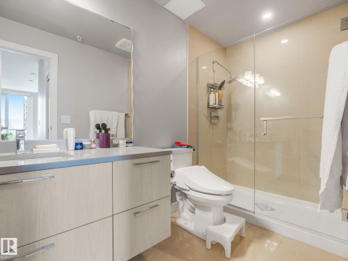 Bathroom featuring a glass-enclosed shower, light-colored wall tiles, recessed lighting, a vanity with a light wood-finish and metal pulls, and a large wall-mounted mirror - #1501 10180 103 St Nw, Edmonton, AB - Indoor Photo Showing Bathroom