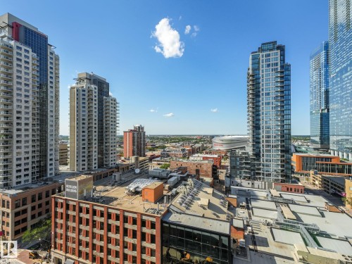 High-rise cityscape featuring modern residential towers with private balconies, commercial buildings with brick facades, and a prominent distant stadium structure - #1501 10180 103 St Nw, Edmonton, AB - Outdoor With Facade