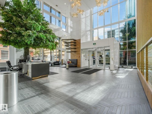 Grand lobby featuring high ceilings, a prominent tree installation, large format herringbone-pattern flooring, extensive window walls, and decorative pendant lighting fixtures - #1501 10180 103 St Nw, Edmonton, AB -  Photo Showing Other Room