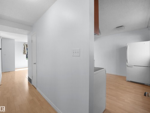 Light wood-finish flooring extending into multiple spaces, white walls, and a white refrigerator - 10446 55 Avenue Nw, Edmonton, AB - Indoor