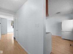 Light wood-finish flooring extending into multiple spaces, white walls, and a white refrigerator - 