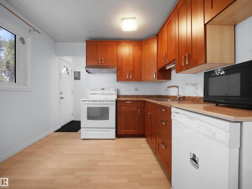 Kitchen featuring wood-finish flooring, white appliances, and warm-toned cabinetry - 10446 55 Avenue Nw, Edmonton, AB - Indoor Photo Showing Kitchen