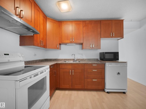 Kitchen featuring wood cabinetry, mottled countertops, and light wood-finish flooring - 10446 55 Avenue Nw, Edmonton, AB - Indoor Photo Showing Kitchen With Double Sink