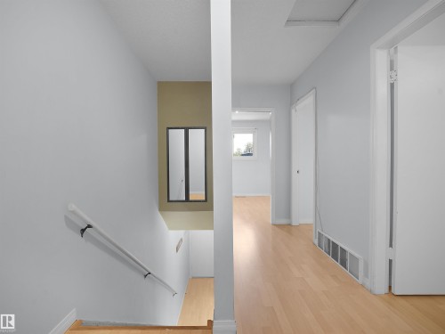 Open hallway featuring wood-finish flooring, light-toned walls, and a staircase with a wall-mounted handrail - 10446 55 Avenue Nw, Edmonton, AB - Indoor Photo Showing Other Room