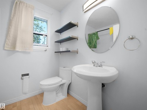 Pedestal sink with chrome faucet, oval mirror, and wall-mounted light fixture - 10446 55 Avenue Nw, Edmonton, AB - Indoor Photo Showing Bathroom