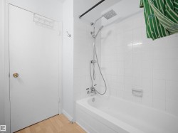 White tiled shower with a rainfall showerhead and handheld sprayer, featuring a built-in tub - 
