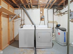 Dedicated laundry area featuring a washer and dryer, exposed ceiling joists, plumbing infrastructure, and a water treatment system - 