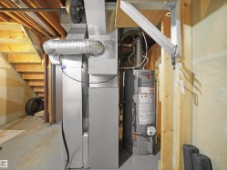 Basement utility area featuring a water heater and furnace with exposed ductwork, concrete flooring, and unfinished wood framing - 