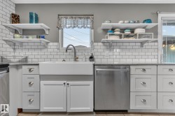 Kitchen featuring a white farmhouse sink with a gooseneck faucet, light gray cabinetry with varied drawer and door configurations, white subway tile backsplash, and granite-style countertops - 