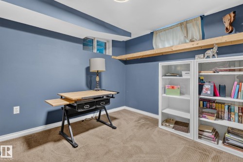 Carpeted room featuring a window, built-in shelving, a full wall shelf, and blue wall paint - 5307 104 Avenue Nw, Edmonton, AB - Indoor Photo Showing Other Room