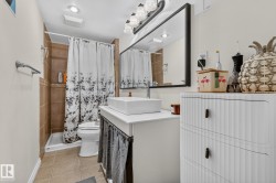 Bathroom featuring a vessel sink, dark framed mirror, and a shower with brown tile surround - 