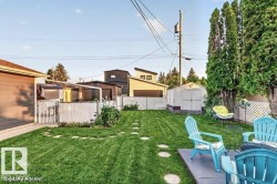 Expansive fenced backyard featuring a manicured lawn, stone paver pathway, and mature privacy trees - 