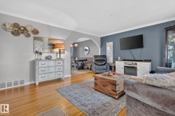 Spacious living area featuring hardwood flooring, crown molding, a built-in media console with an electric fireplace, an arched entryway, and recessed lighting in the dining area - 