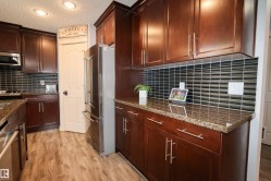 Kitchen featuring cherry wood-finish cabinetry, stainless steel appliances, dark horizontal tile backsplash, light wood-finish flooring, and recessed ceiling lighting - 
