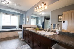 Bathroom featuring a dual vanity with a dark wood-finish cabinet and stone-look countertop, an integrated bathtub with a tiled surround, a large window, and patterned flooring - 