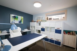 Dedicated workspace featuring a large desk with a blue desktop mat, ample built-in shelving, and a prominent window - 