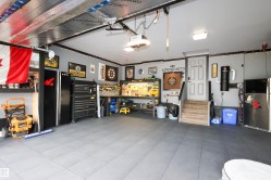 Spacious garage featuring durable tile flooring, painted walls, overhead lighting, a built-in workbench, and a service door with stairs - 