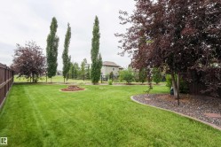 Expansive backyard featuring a lush lawn, mature trees, a decorative rock bed, and a wooden privacy fence - 