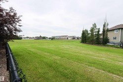 Expansive green space featuring a chain-link fence, mature trees, and a residential structure with neutral siding - 