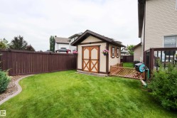 Manicured backyard featuring a storage shed with wood doors and window shutters, a brown privacy fence, green lawn, and a decorative concrete border - 