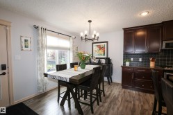 Open-concept living area featuring wood-finish flooring, dark wood cabinetry, a dark tile backsplash, and recessed lighting - 