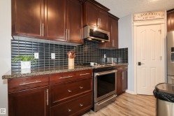 Kitchen featuring dark wood-finish cabinetry with silver-tone hardware, granite-look countertops, and a black subway tile backsplash - 