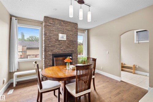 Interior dining area featuring wood-finish flooring, a stacked stone fireplace with a black insert, and a contemporary linear pendant light fixture - 11719 127 Street Nw, Edmonton, AB - Indoor Photo Showing Dining Room