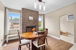 Interior dining area featuring wood-finish flooring, a stacked stone fireplace with a black insert, and a contemporary linear pendant light fixture - 