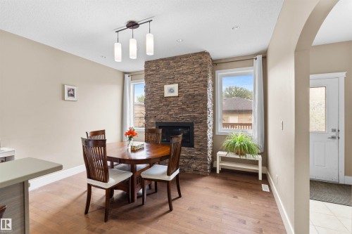 Inviting dining area featuring a stacked stone fireplace, wood-finish flooring, and a modern linear pendant light fixture - 11719 127 Street Nw, Edmonton, AB - Indoor Photo Showing Dining Room With Fireplace