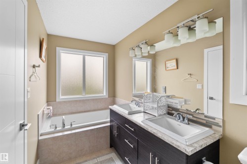 Bathroom featuring a built-in bathtub with tiled surround, a frosted window, and a dual vanity with undermount sinks and a full-width mirror - 11719 127 Street Nw, Edmonton, AB - Indoor Photo Showing Bathroom