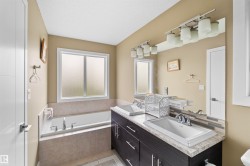 Bathroom featuring a built-in bathtub with tiled surround, a frosted window, and a dual vanity with undermount sinks and a full-width mirror - 