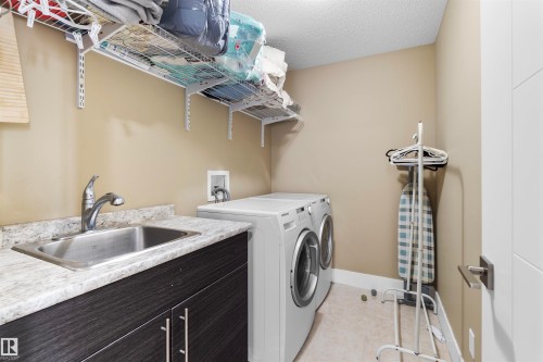 Dedicated laundry area featuring a stainless steel sink, wood-finish cabinetry, and a light-toned countertop - 11719 127 Street Nw, Edmonton, AB - Indoor Photo Showing Laundry Room