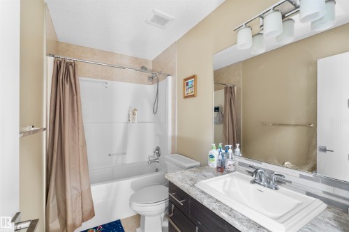 Bathroom featuring a white tub with shower, beige tiled surround, and a dark wood-finish vanity with a white rectangular sink - 11719 127 Street Nw, Edmonton, AB - Indoor Photo Showing Bathroom