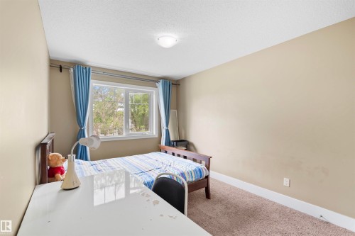 Bedroom featuring a large window with white trim, neutral wall paint, white baseboards, and textured carpet flooring - 11719 127 Street Nw, Edmonton, AB - Indoor Photo Showing Bedroom