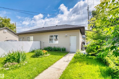 Rear exterior featuring light beige siding, a dark shingle roof, a white access door, and a single window - 11719 127 Street Nw, Edmonton, AB - Outdoor