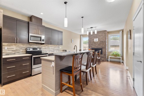 Contemporary kitchen featuring wood-finish cabinetry, stainless steel appliances, a tile backsplash, and a breakfast bar island - 11719 127 Street Nw, Edmonton, AB - Indoor Photo Showing Kitchen With Upgraded Kitchen