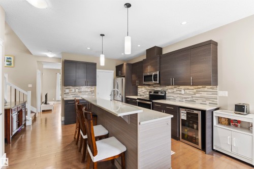 Modern kitchen featuring wood-finish flooring, dark wood-finish cabinetry, light-toned countertops, a full stainless steel appliance package, and a beverage refrigerator - 11719 127 Street Nw, Edmonton, AB - Indoor Photo Showing Kitchen With Upgraded Kitchen